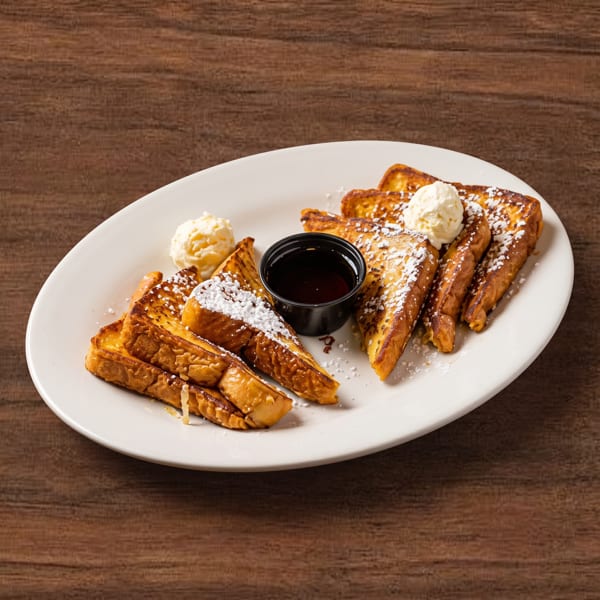 Golden french toast slices on a white plate with powdered sugar, butter, and a side of syrup.